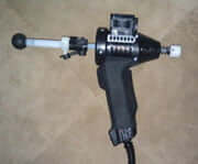 arthrostim - chiropractor tool A close-up of a handheld power tool with a black handle and a cylindrical attachment extending from the front, lying on a beige surface. The tool appears to be custom-built.